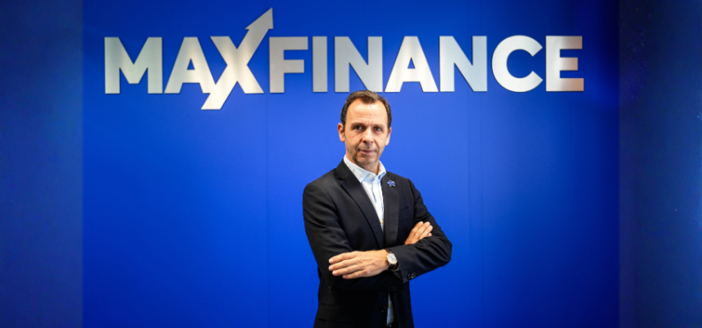 CEO Maxfinance de braços cruzados em fundo azul com logotipo
